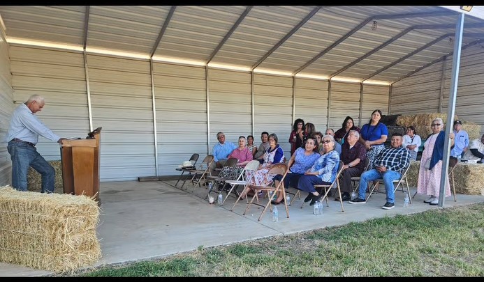 Pastor speaking at the podium with the congregation seated outdoors under the covered area